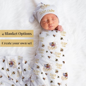 May include: A baby swaddled in a white blanket and wearing a matching hat, decorated with bees and flowers. The name "Olivia Chloe" is printed in gold. The image also includes text that says "4 Blanket Options" and "Create your own set".