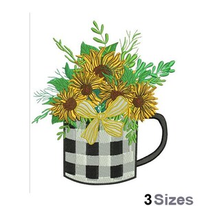 Op de afbeelding: Borduurwerk van een zwart-wit geblokte mok gevuld met een boeket gele zonnebloemen en groene bladeren. De mok heeft een gele strik en een zwart handvat.