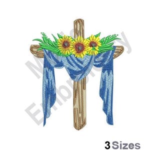 May include: A wooden cross with a blue fabric draped over it. The cross is decorated with sunflowers and green leaves.