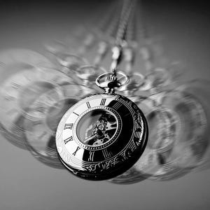 Può includere: Un orologio da tasca argentato con numeri romani sul quadrante e un meccanismo interno visibile. L'orologio è appeso a una catena ed è sfocato sullo sfondo.