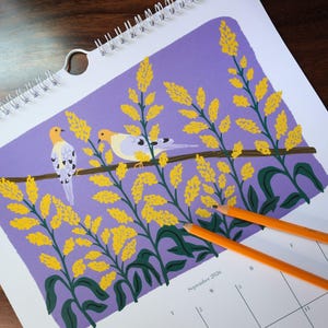 May include: A calendar with a spiral binding, displaying an illustration of two birds on a branch surrounded by yellow flowers against a purple background. The calendar page shows September 2020, with two orange pencils on the page.