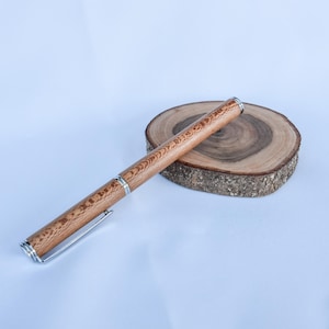 Könnte beinhalten: Ein Holzstift mit silbernen Details liegt auf einer kleinen, runden Holzscheibe. Der Stift hat eine hellbraune Oberfläche mit einem Holzmaserungsmuster. Die Holzscheibe hat eine dunkelbraune Mitte und einen helleren braunen Rand.