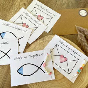 Può includere: Biglietti bianchi con scritte nere che chiedono "Vuoi essere la mia damigella d'onore?" e "Vuoi essere il mio padrino?" con illustrazioni di buste e pesci. Sono presenti anche una busta marrone e perline decorative.