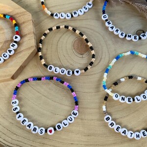 Puede incluir: Seis pulseras de cuentas con letras blancas que forman frases como DUNCAN, ALL RISE, U MAKE ME WANNA, BLUE, 25 YEARS BLUE, ONE LOVE y BREATHE EASY. Las pulseras están hechas de cuentas de vidrio de colores y cuentas de letras negras y blancas.