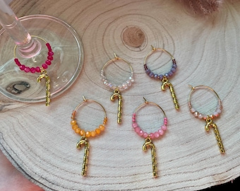 May include: A set of six circular wine glass charms featuring gold-toned metal candy cane charms. Each hoop is decorated with small, faceted beads in various colors including bright pink, orange, light pink, purple, and soft peach tones.