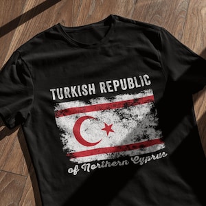 Könnte beinhalten: Schwarzes T-Shirt mit einem abgenutzten weißen Grafikdruck der Flagge der Türkischen Republik Nordzypern. Die Grafik enthält den Text "Turkish Republic of Northern Cyprus".