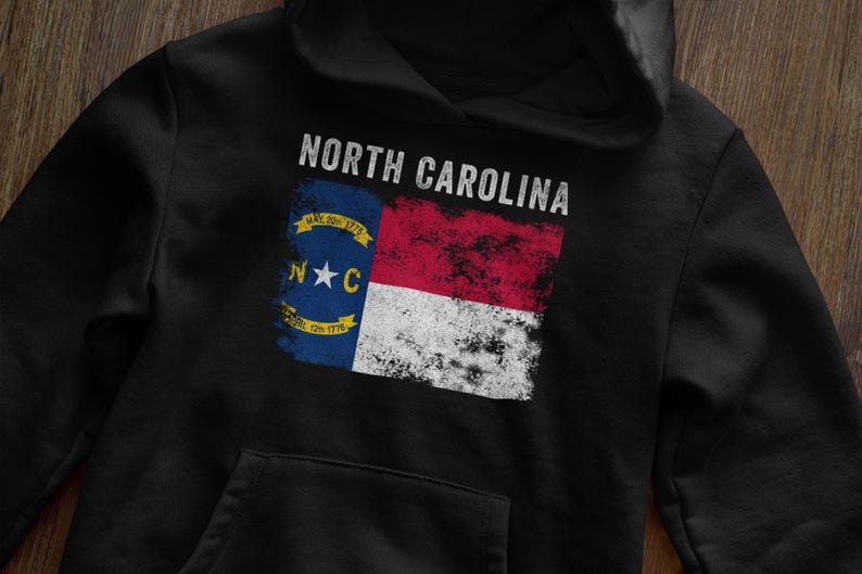 May include: Black hoodie with a distressed North Carolina flag graphic. The flag features the state seal with the text "May 20th 1775" and "April 12th 1776".