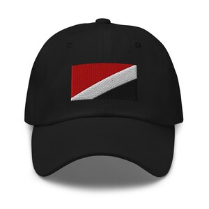 Może przedstawiać: Czarna czapka z daszkiem z haftowaną flagą Trynidadu i Tobago. Flaga jest czerwona, biała i czarna.
