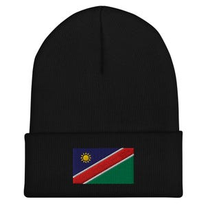 Op de afbeelding: Zwarte beanie met een klein geborduurd vlaggetje van Namibië op de voorkant. De vlag is blauw, rood en groen met een gele zon in de linkerbovenhoek.