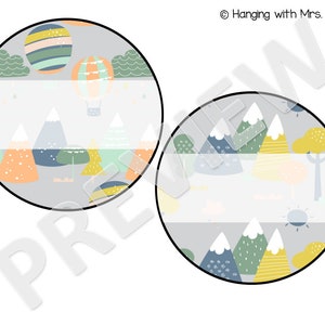 May include: Two round printable labels with a mountain and hot air balloon theme. The labels feature a gray background with colorful mountains, trees, and clouds. The top label has a hot air balloon with stripes and a basket. The bottom label has a sun and a tree. Both labels have a blank space for text.