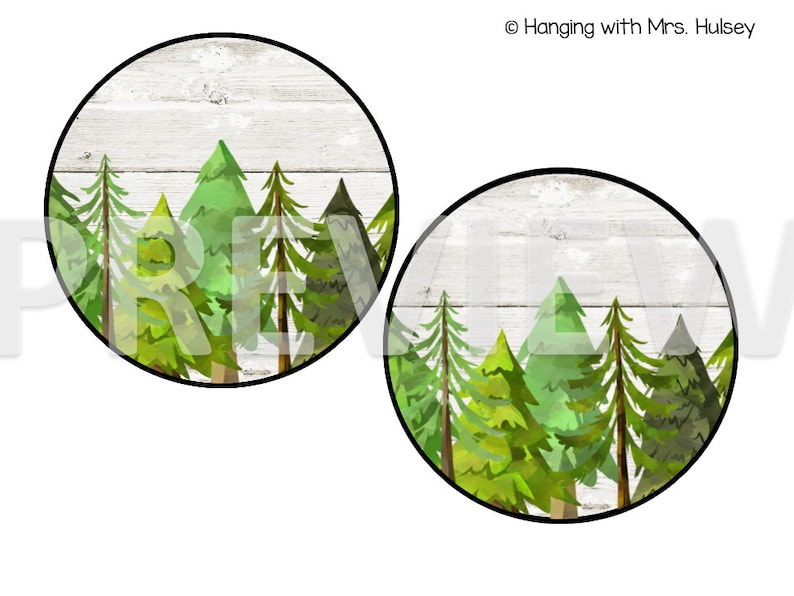 May include: Two round wood-grain stickers with a watercolor illustration of a forest scene. The stickers feature a row of green pine trees against a white wood background.
