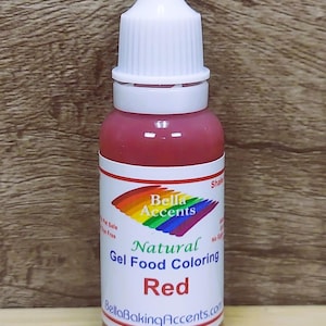May include: A bottle of red gel food coloring with a white cap and label. The label features a rainbow design and the words "Bella Accents Natural Gel Food Coloring Red". The bottle is against a wooden background.