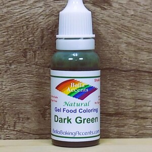 May include: A bottle of dark green gel food coloring with a white cap and a label featuring a rainbow design and the text "Bella Accents Natural Gel Food Coloring Dark Green". The bottle is on a wooden background.