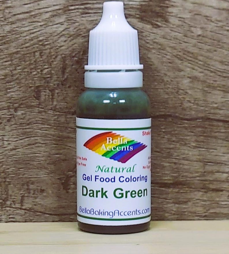 May include: A bottle of dark green gel food coloring with a white cap and a label featuring a rainbow design and the text "Bella Accents Natural Gel Food Coloring Dark Green". The bottle is on a wooden background.