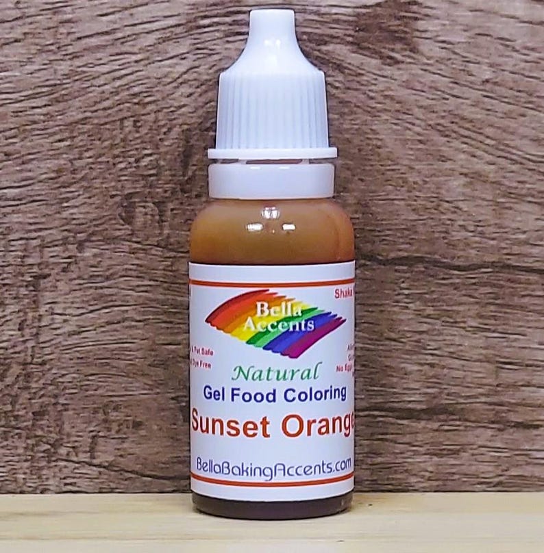 May include: A bottle of Sunset Orange gel food coloring by Bella Accents. The bottle has a white cap and a label with a rainbow design and the words "Natural Gel Food Coloring". The bottle is filled with an orange liquid.