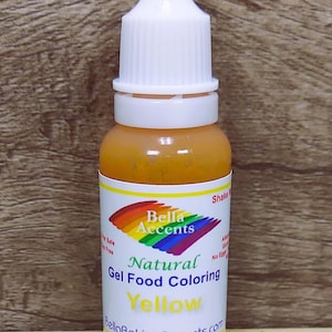 May include: A bottle of yellow natural gel food coloring. The label features the brand name "Bella Accents" with a rainbow design. The bottle has a white cap and is filled with a yellow liquid. The text "Yellow" is prominently displayed on the label.