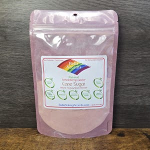 May include: A clear, resealable stand-up pouch containing pink strawberry caster cane sugar. The label features a rainbow graphic, the text Bella Accents, Natural Strawberry Caster Cane Sugar, and Net Wt. 4oz (113g) with various green circular icons.