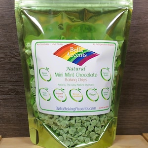 May include: A green metallic bag filled with mini mint chocolate baking chips. The bag has a label with the text "Bella Accents" and "Natural Mini Mint Chocolate Baking Chips". The label also includes icons for gluten-free, vegan, and minimal ingredients.