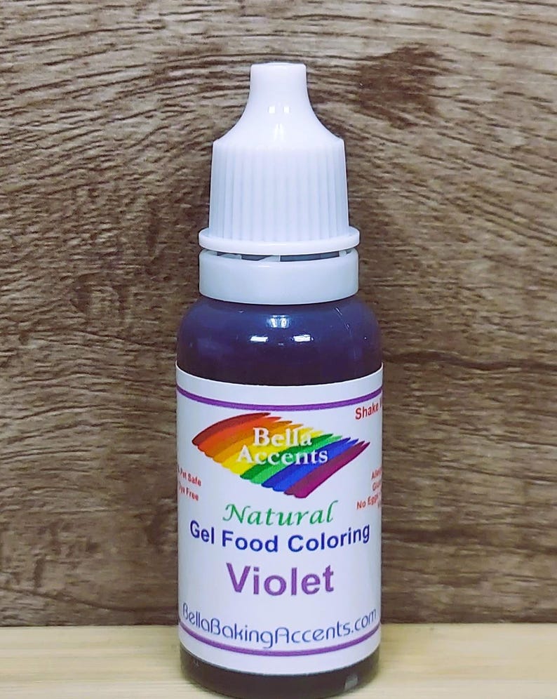 May include: A bottle of violet-colored natural gel food coloring. The bottle has a white cap and a label with the text "Bella Accents" and "Natural Gel Food Coloring Violet". The label also includes a rainbow design.