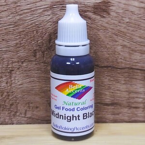 May include: A bottle of natural gel food coloring labeled "Midnight Black" by Bella Accents. The bottle has a white cap and a label with a rainbow design. The dark liquid is visible through the clear glass.