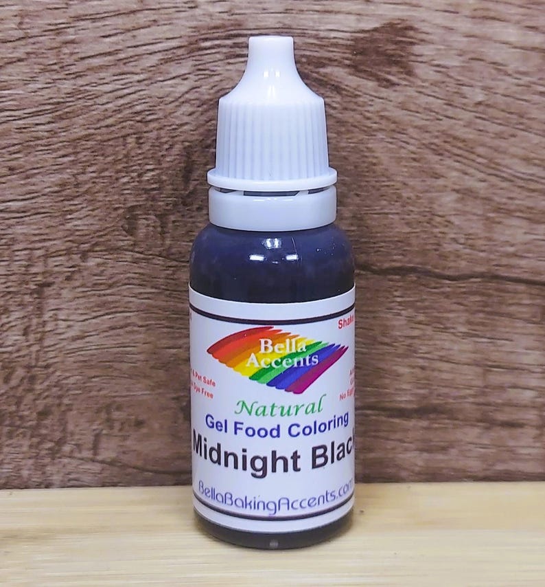 May include: A bottle of natural gel food coloring labeled "Midnight Black" by Bella Accents. The bottle has a white cap and a label with a rainbow design. The dark liquid is visible through the clear glass.