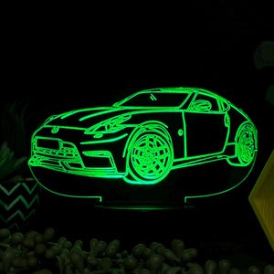 May include: A green 3D printed acrylic night light shaped like a sports car. The night light is illuminated from the inside, creating a glowing outline of the car.