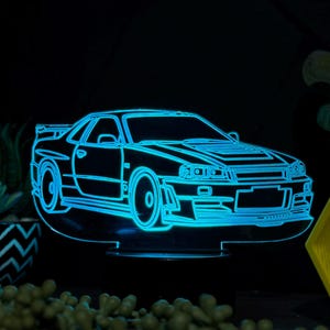 May include: A blue 3D printed night light shaped like a Nissan Skyline R34 car. The light is on and illuminating the car.