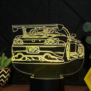 May include: A yellow 3D printed night light shaped like a car with a spoiler and the word "WIPS" on the license plate. The night light is on a black base and is lit up.