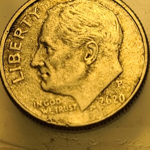 May include: A close-up of a 2020 United States dime. The coin features a profile of Franklin D. Roosevelt, the word "LIBERTY", and the phrase "IN GOD WE TRUST". The coin is gold in colour.