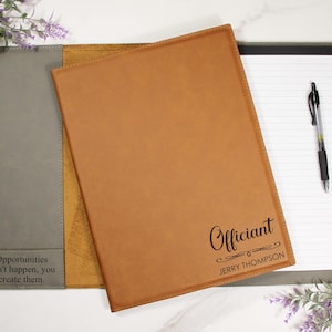 May include: A brown leather portfolio with the word "Officiant" and the name "Jerry Thompson" engraved on the front. The portfolio is open, revealing a notepad and pen. A gray portfolio with the text "Opportunities don't happen, you create them" is also visible.