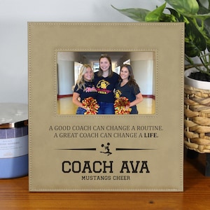 May include: Tan picture frame with a photo of three people. The frame has the text "A GOOD COACH CAN CHANGE A ROUTINE. A GREAT COACH CAN CHANGE A LIFE." and "COACH AVA MUSTANGS CHEER."
