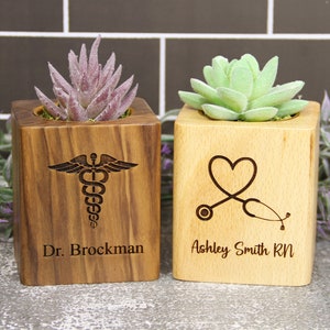 May include: Two wooden planter boxes with succulents. The box on the left has a medical symbol and the text "Dr. Brockman". The box on the right has a heart and stethoscope symbol and the text "Ashley Smith RN".