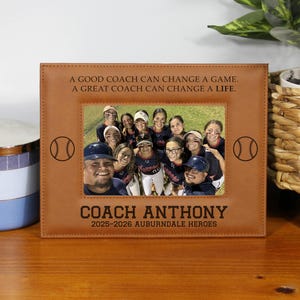 May include: A brown leather picture frame with a team photo. The frame has the text "A GOOD COACH CAN CHANGE A GAME. A GREAT COACH CAN CHANGE A LIFE." and "COACH ANTHONY 2025-2026 AUBURNDALE HEROES."