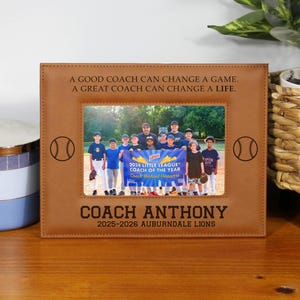 May include: A brown leather picture frame with a team photo, baseball graphics, and text. The text reads "A GOOD COACH CAN CHANGE A GAME. A GREAT COACH CAN CHANGE A LIFE." and "COACH ANTHONY 2025-2026 AUBURNDALE LIONS."