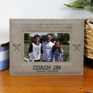 May include: A rectangular, light brown picture frame with a photo of three people. The frame has the text "A GOOD COACH CAN CHANGE A GAME. A GREAT COACH CAN CHANGE A LIFE." and "COACH JIM FEEHAN LACROSSE."