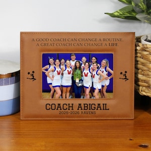 May include: A brown picture frame with a photo of a cheerleading team. The frame has the text "A GOOD COACH CAN CHANGE A ROUTINE. A GREAT COACH CAN CHANGE A LIFE." and "COACH ABIGAIL 2025-2026 RAVENS."