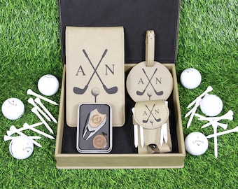 Peut inclure: Coffret cadeau de golf avec un carnet, une étiquette de bagage et une pochette en similicuir beige, tous ornés de clubs de golf croisés et des initiales "A N". Comprend des balles de golf, des tees et un outil de réparation de divot. Sur fond vert.