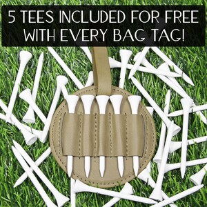 May include: A golf bag tag with a holder for golf tees, surrounded by white golf tees on a green grass background. The bag tag is tan and holds five white golf tees. Text at the top reads "5 TEES INCLUDED FOR FREE WITH EVERY BAG TAG!"