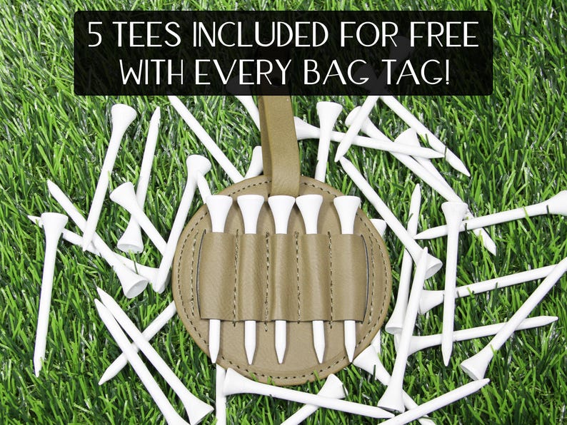 May include: A golf bag tag with a holder for golf tees, surrounded by white golf tees on a green grass background. The bag tag is tan and holds five white golf tees. Text at the top reads "5 TEES INCLUDED FOR FREE WITH EVERY BAG TAG!"