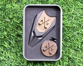 May include: A silver metal golf ball marker and a golf club tool in a gray box. Both items have a wooden inlay with the letters "A" and "V" and crossed golf clubs.