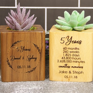 May include: Two wooden planter boxes with engraved text celebrating a 5 year anniversary. The left box has a floral wreath design with the names "Daniel & Sydney" and the date "05.11.18". The right box has the text "5 Years" and lists the number of months, weeks, days, hours, and minutes in 5 years. It also includes the text "countless memories" and the names "Jake & Steph" with the date "05.11.18".