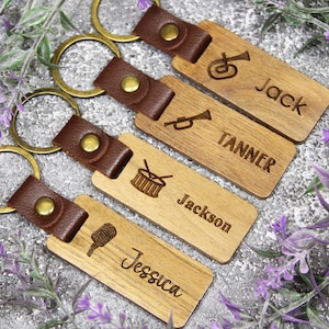 Puede incluir: Cuatro llaveros de madera con correas de cuero marr&oacute;n y aros dorados. Cada llavero est&aacute; grabado con un nombre y un instrumento musical: Jack con una tuba, Tanner con una trompeta, Jackson con un tambor y Jessica con un micr&oacute;fono.