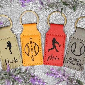 May include: Four leather baseball keychains in tan, orange, red, and gray. Each keychain has a gold ring and features a baseball-themed design with a name or title: Nick, Tristan, Mike, and Coach Dallas.