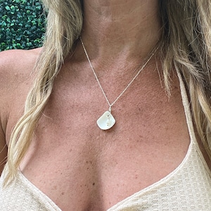 Puede incluir: Una mujer con un top halter de color crema con un collar de cadena de plata y un colgante de concha blanca.