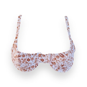 May include: White bikini top with a brown cowboy-themed pattern. The pattern includes cowboy boots, cacti, horseshoes, and stars. The top has adjustable straps and a classic underwire design.