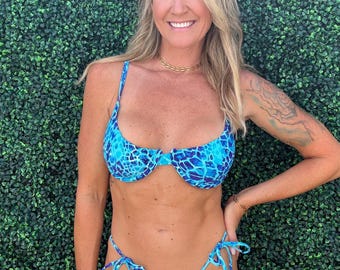 Puede incluir: Conjunto de bikini azul con un patrón único. La parte superior presenta soporte de aros y tirantes ajustables. La parte inferior es de estilo tanga con cierres de lazo. El traje de baño está hecho de una tela azul vibrante con un diseño texturizado.