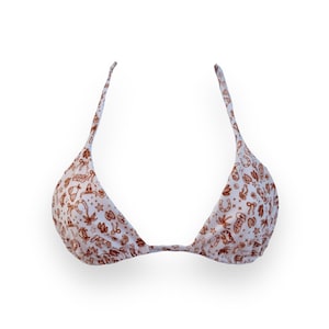 May include: A white bikini top with a brown pattern of cowboy-themed illustrations. The top features adjustable straps and a triangle shape. The pattern includes stars, horseshoes, and cowboy hats.