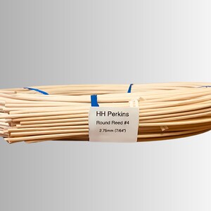 May include: A bundle of round reeds, tied with blue tape. The label reads "HH Perkins Round Reed #4 2.75mm (7/64")". The reeds are a light beige color and appear to be made of natural material. The reeds are coiled.