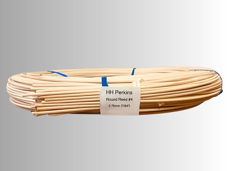 May include: A bundle of round reeds, tied with blue tape. The label reads "HH Perkins Round Reed #4 2.75mm (7/64")". The reeds are a light beige color and appear to be made of natural material. The reeds are coiled.