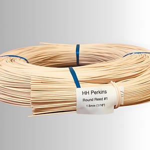 May include: A coil of natural-colored round reed, secured with blue bands. A label reads "HH Perkins Round Reed #1 1.5mm (1/16")". The reed is tightly wound, suggesting its use in weaving or crafting projects.